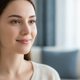 Portrait of a serene young woman with clear skin, smiling gently, conveying comfort and satisfaction in a peaceful home setti